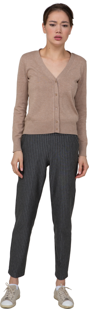 Vista frontal de uma jovem perplexa parada, usando um pulôver e calças parecendo em linha reta