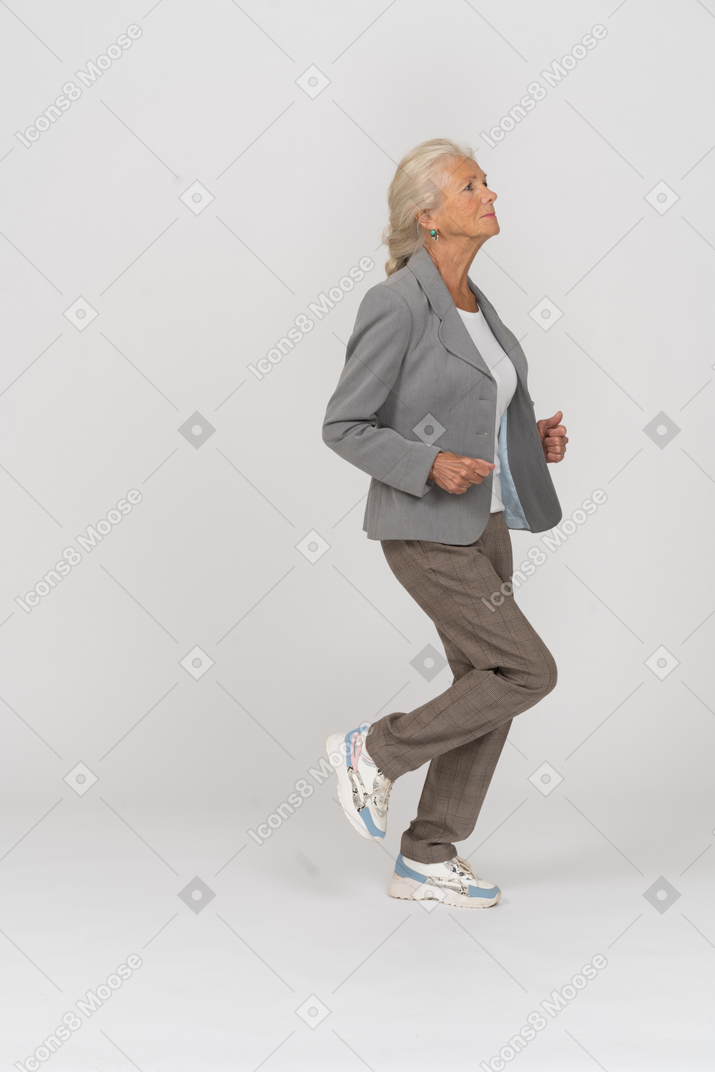 Vista laterale di una vecchia signora in completo che corre