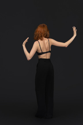 A backside view of the cute young woman dancing on the black background