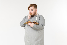 Um homem gordo comendo um cookie com olhar culpado