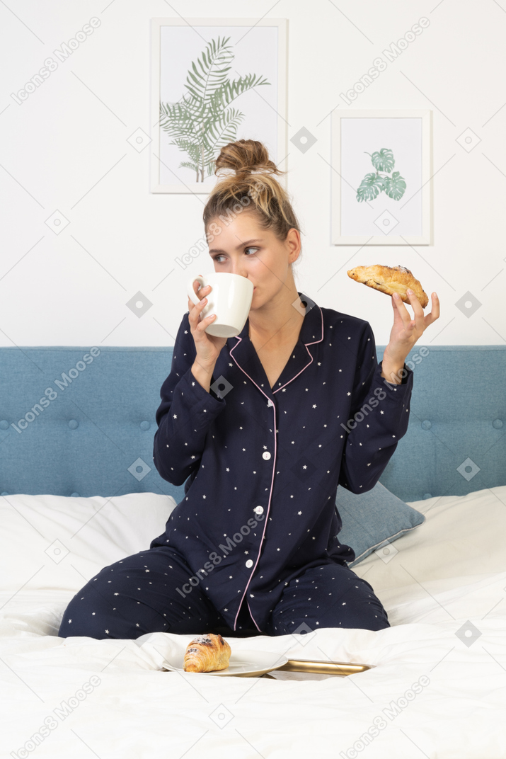 Вид спереди молодой леди в пижаме, завтракающей в постели