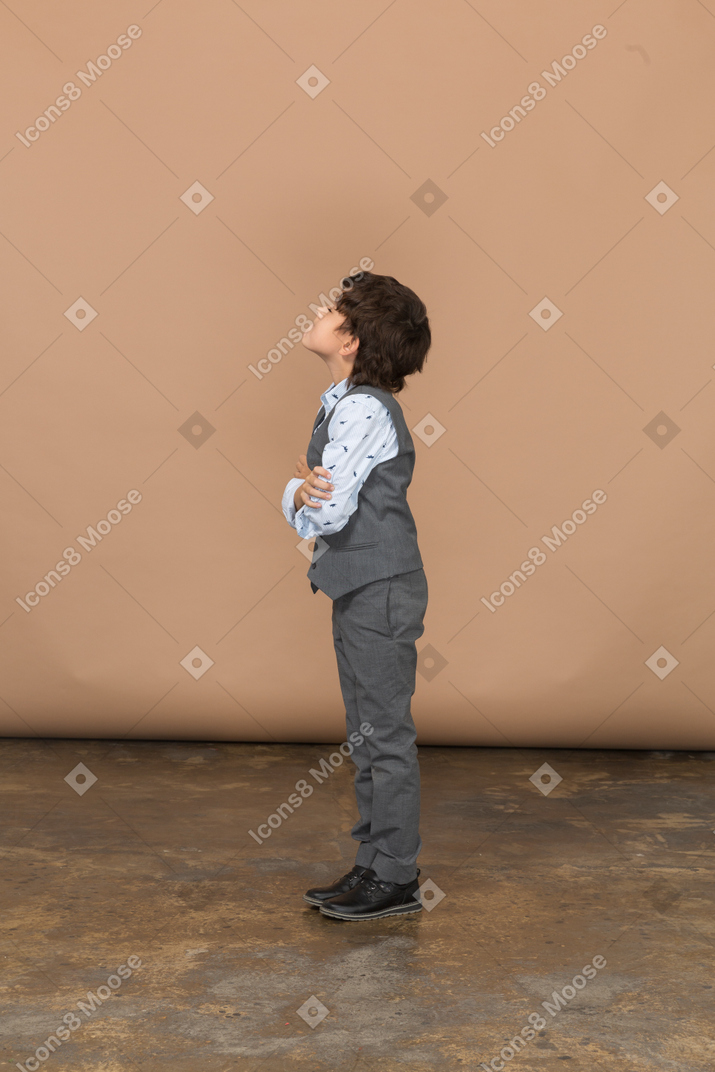Vista lateral de un niño con traje gris abrazándose a sí mismo