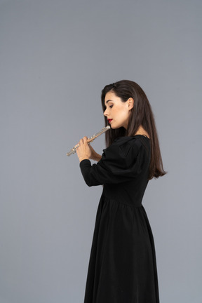 Side view of a serious young lady in black dress playing the flute