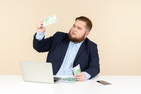 Young overweight man making sure money bills are real ones