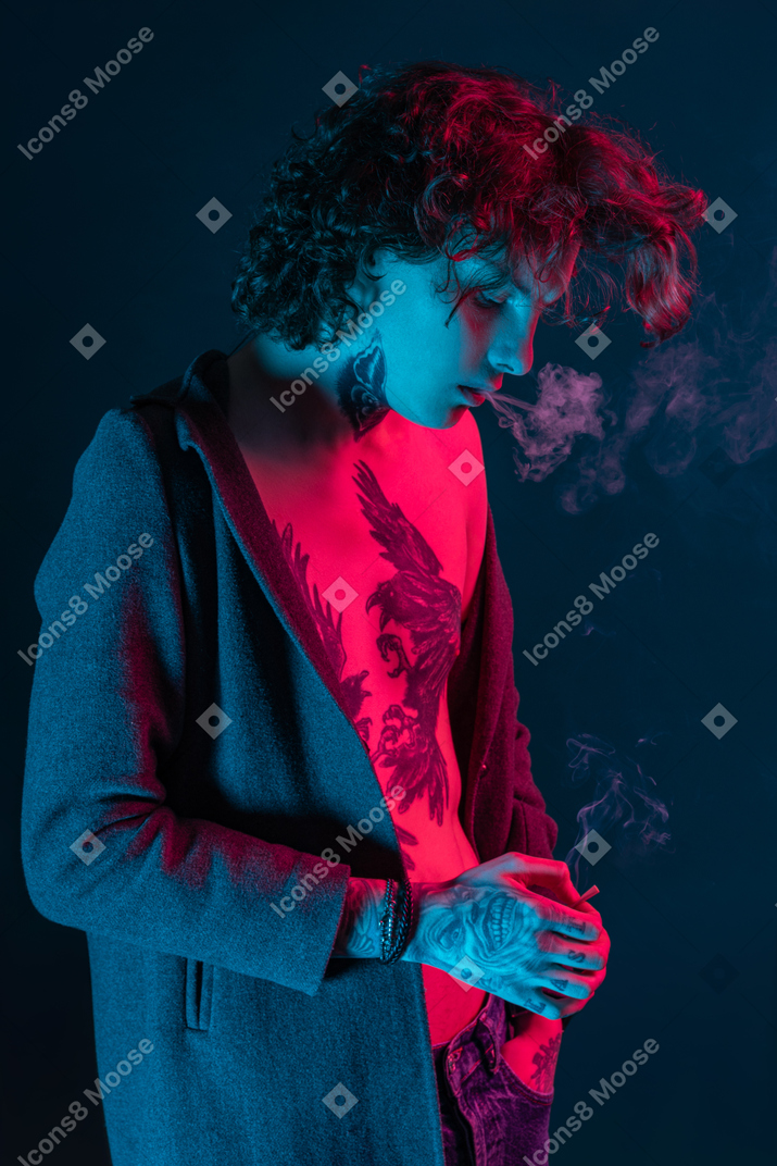 Male in jacket smokes under neon lights