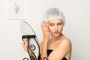 Young woman tightening her face skin while looking in the mirror