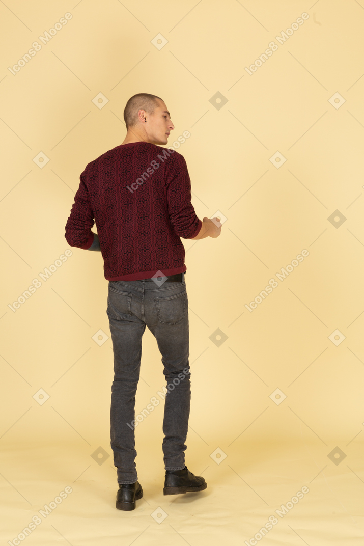 Back view of a gesticulating young curious man in red pullover