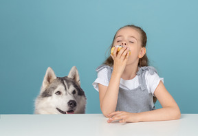 Nettes kleines mädchen, das einen krapfen und einen heiseren hund betrachten sie isst