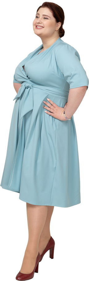 Вид спереди счастливой женщины в голубом платье, стоящей с руками на бедрах
