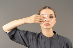 Vista frontal de una mujer joven en un mono quitando el maquillaje de ojos