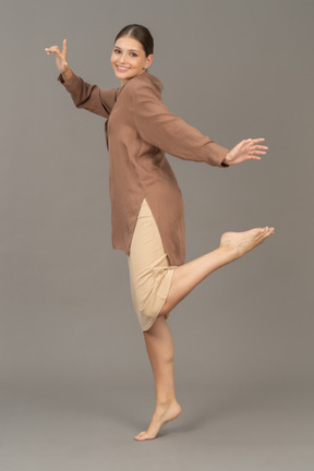 Vista laterale di una donna in piedi a piedi nudi in punta di piedi con la gamba sollevata