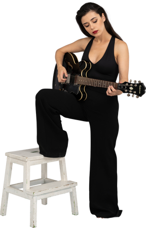 Vista de três quartos de uma jovem de terno preto segurando o violão e colocando a perna no banquinho