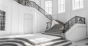 Una hermosa sala vacía con una escalera calada y grandes ventanas blancas.