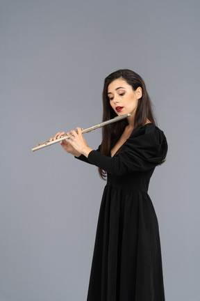 Three-quarter view of a serious young lady in black dress playing the flute