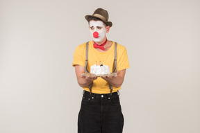 Male clown tasting a cake he's holding