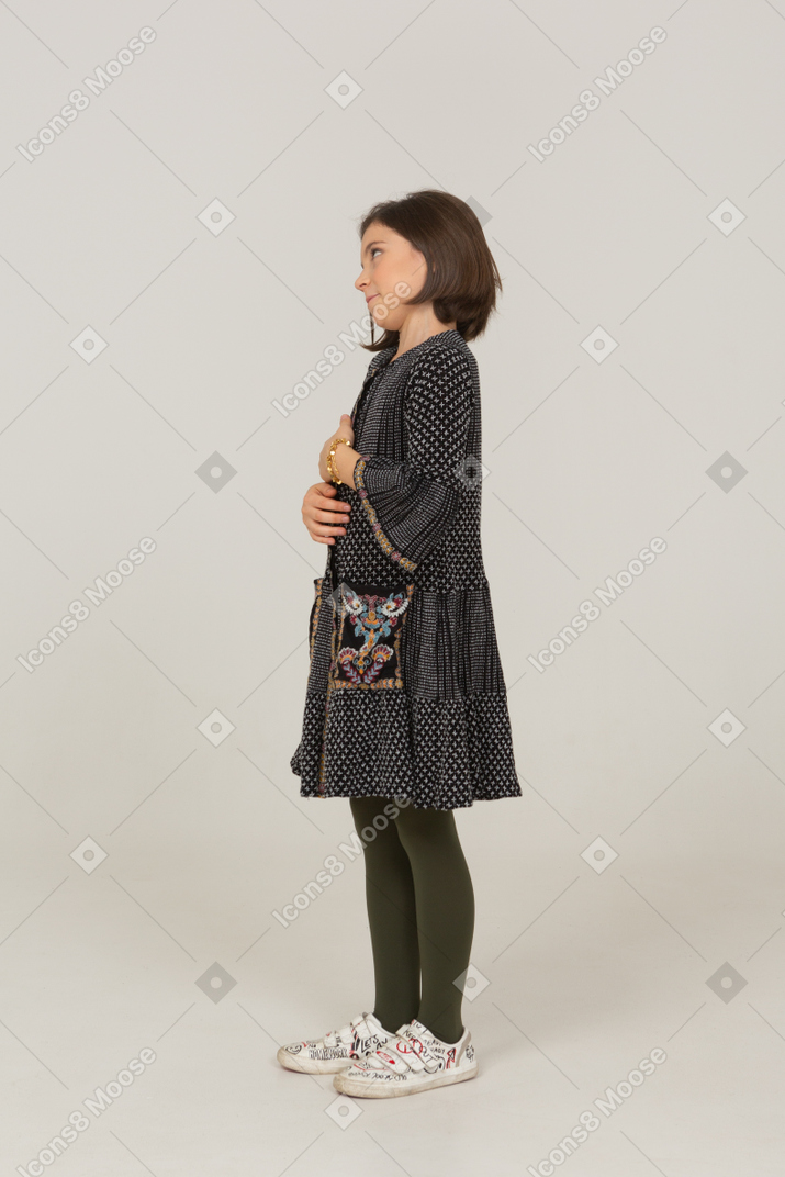 Vista laterale di una bambina in abito che guarda da parte e si tiene per mano insieme