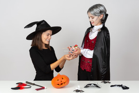 Ragazzo in costume da vampiro che mostra un mucchio di caramelle alla mamma