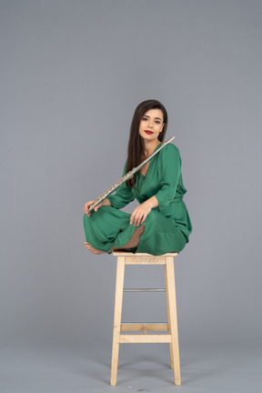 Девушка в полный рост, держащая кларнет, сидящая со скрещенными ногами на деревянном стуле