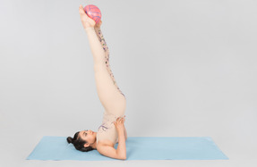 Young indian gymnast lying on yoga mat on the back and holding ball up with legs