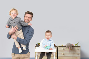 Man holding a baby in his arms next to a baby in highchair