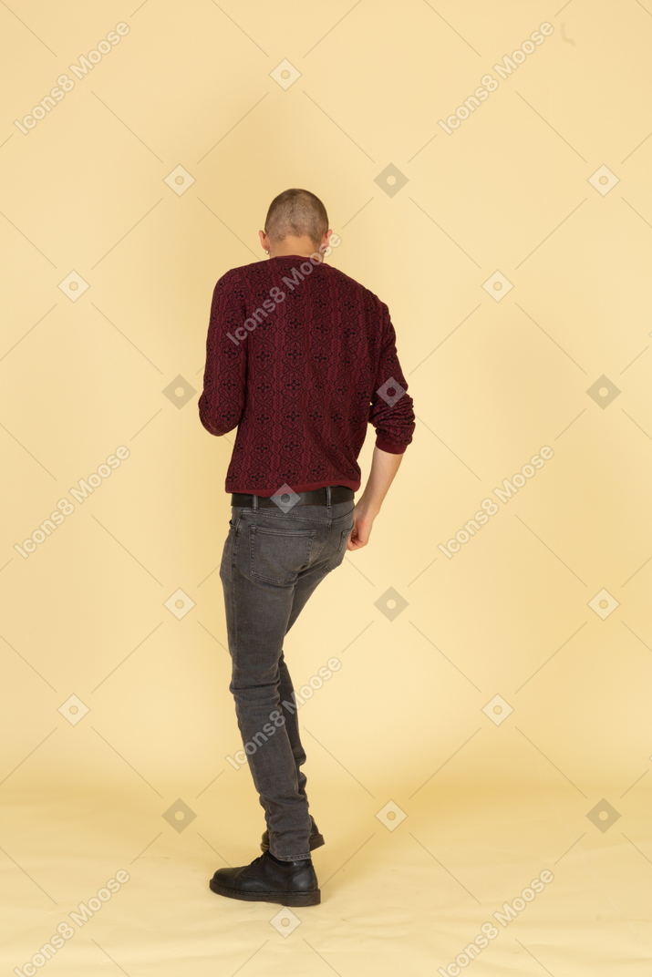 Vista posteriore di un giovane uomo danzante in pullover rosso alzando la gamba
