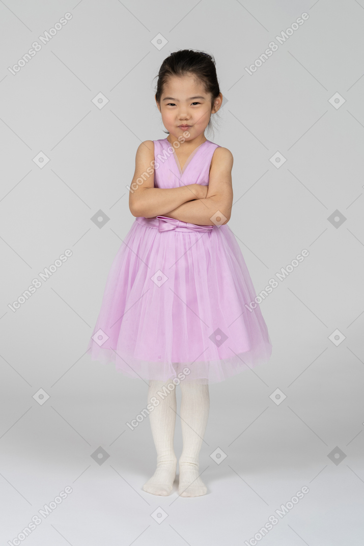 Moody little girl in pink dress standing with arms crossed