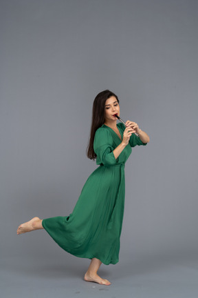 Seitenansicht einer barfüßigen jungen dame im grünen kleid, die flöte spielt