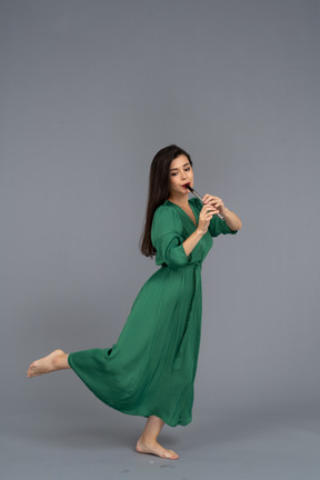 Side view of a barefooted young lady in green dress playing the flute