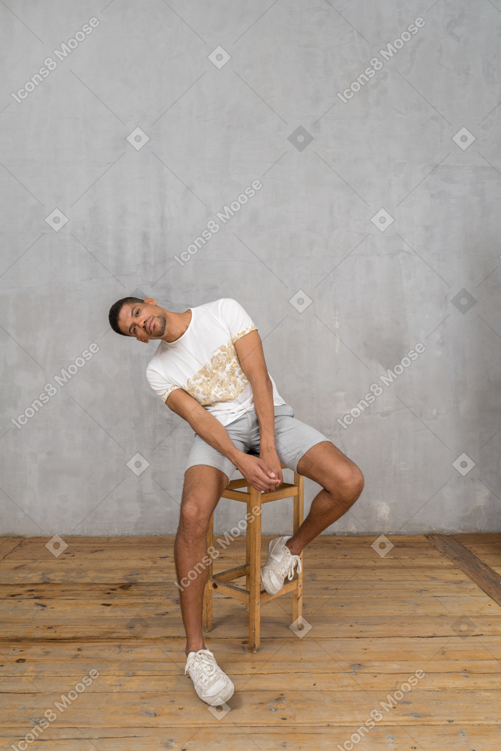 Молодой человек сидит и наклоняется боком