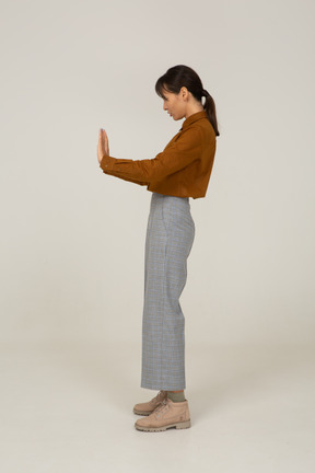 Vista laterale di una giovane donna asiatica in calzoni e camicetta che allunga il braccio