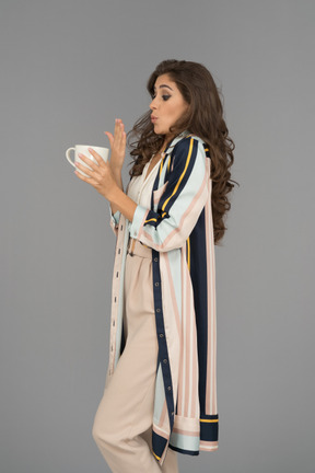 Young woman holding a hot cup of tea and blowing on her right hand