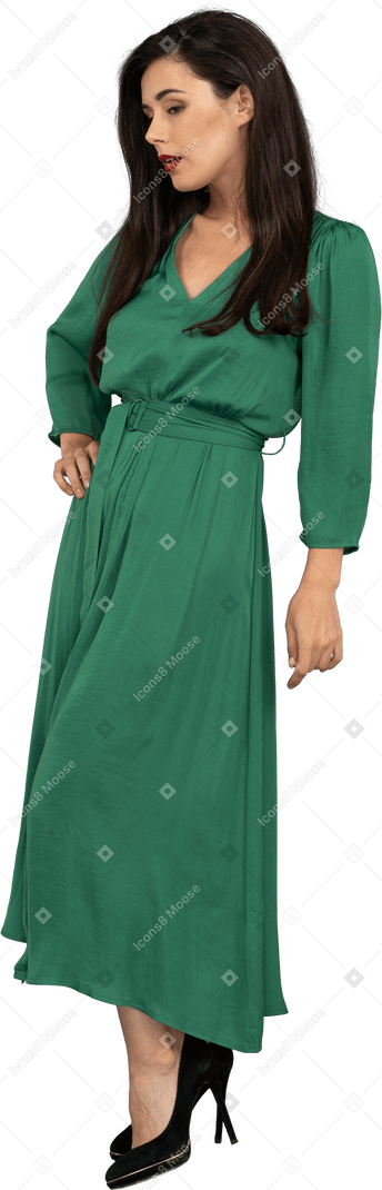 Vue de trois quarts d'une jolie jeune femme en robe verte mettant la main sur la hanche