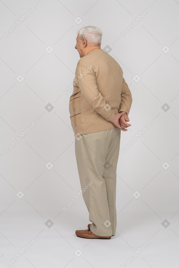 Side view of an old man in casual clothes posing with hands behind back