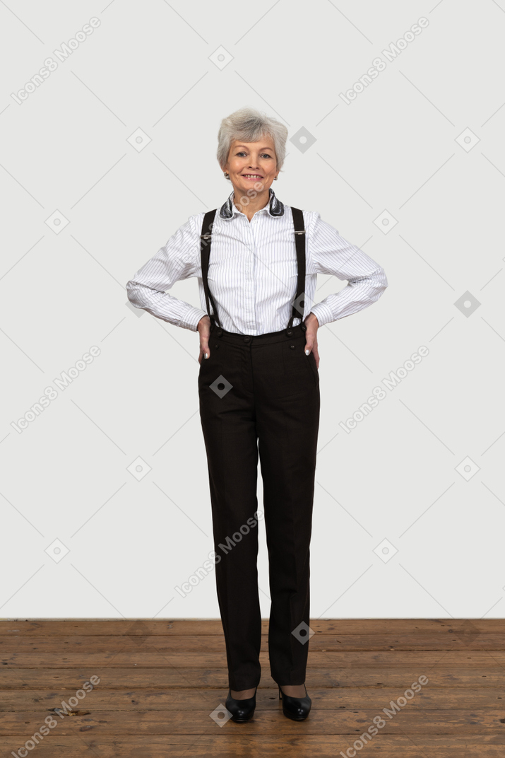Figura intera di una donna anziana felice in bretelle che mette le mani sui fianchi