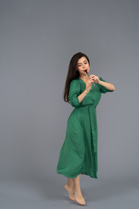 Three-quarter view of a walking young lady in green dress playing the flute