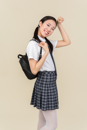Asian school girl with backpack standing in profile and holding fist next to her forehead