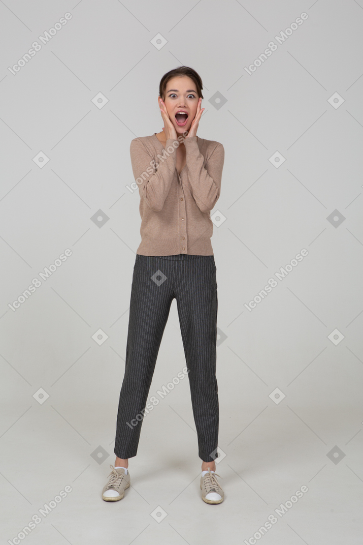 Front view of a surprised young lady in beige pullover touching her face