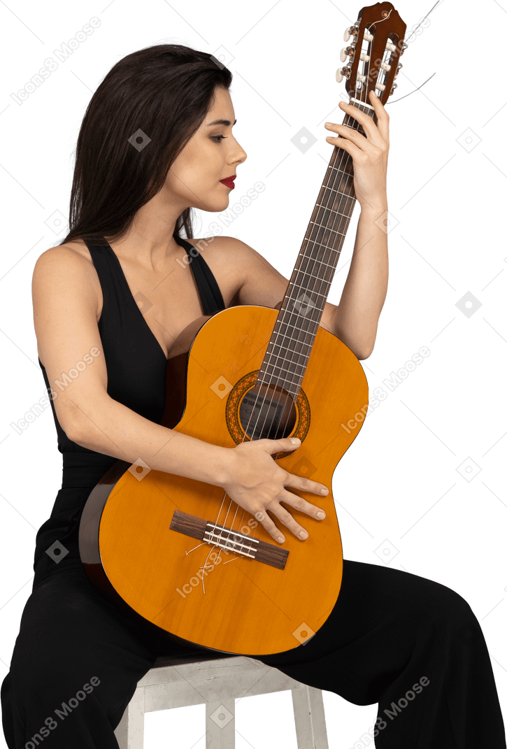 Front view of a sitting young lady in black suit looking at her guitar