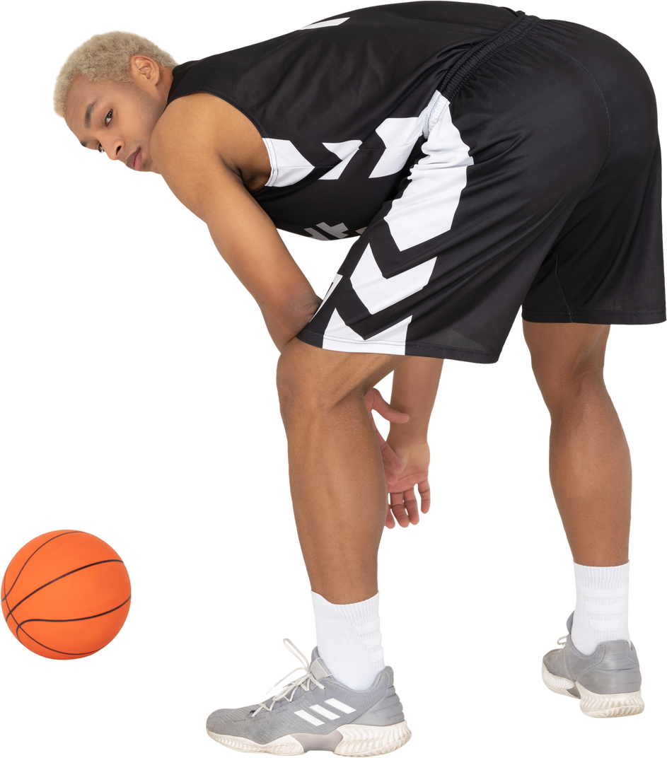 Three-quarter back view of a young male basketball player standing by the ball