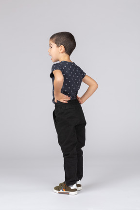 Vue latérale d'un mignon petit garçon debout avec les mains sur les hanches