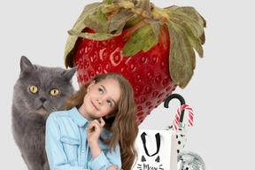 Bambina che sogna ad occhi aperti con gatto grigio, fragola e bastoncini di zucchero sullo sfondo