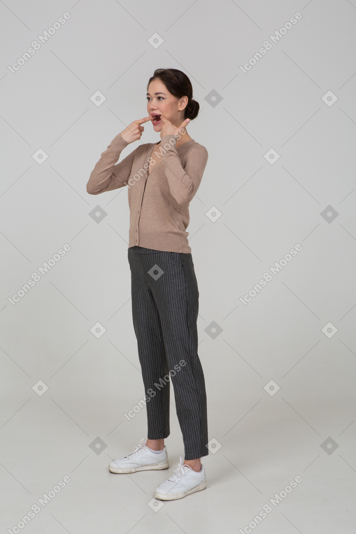 Three-quarter view of a young lady in pullover and pants touching her mouth