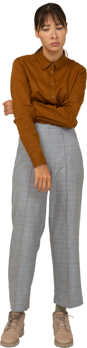 Vista frontal de uma jovem mulher asiática retraída de calça e blusa tocando a barriga