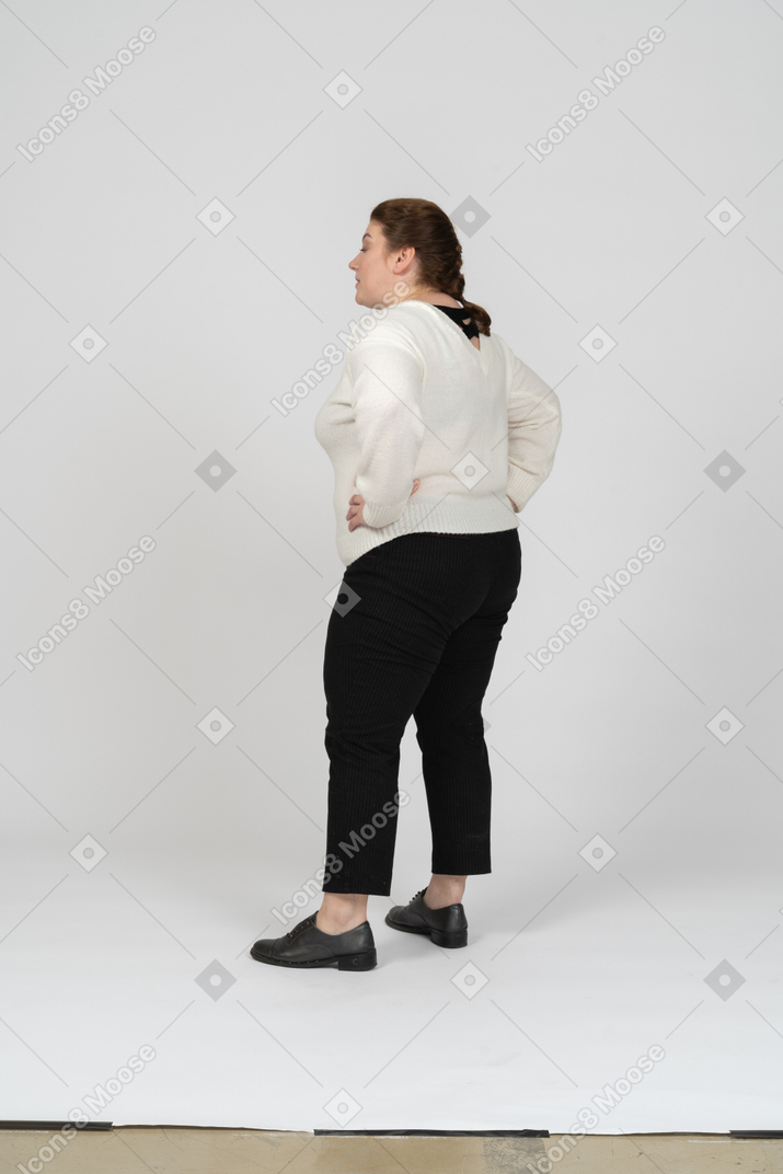 Вид сзади пухлой женщины в повседневной одежде, стоящей с руками на бедрах