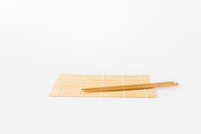 Bamboo mat with chopsticks on it on white background