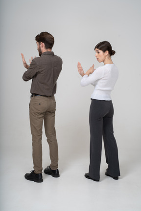 Vista posterior de tres cuartos de una joven pareja en ropa de oficina cruzando los brazos