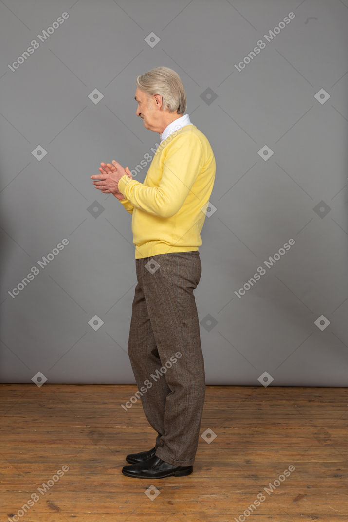 Side view of an applauding old man in a yellow pullover looking aside