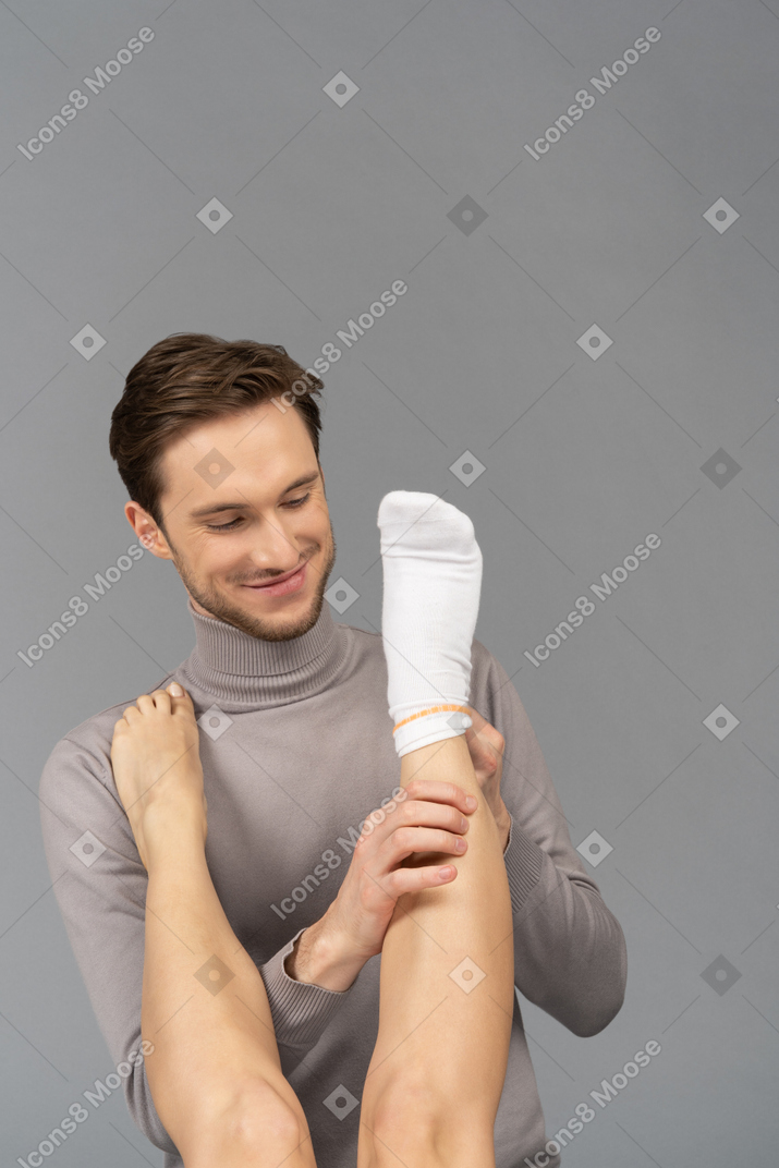Ein fröhlicher junger mann, der eine weiße socke am fuß der frau trägt