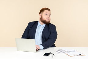 Молодой офисный работник с избыточным весом сидит за офисным столом и смотрит через плечо