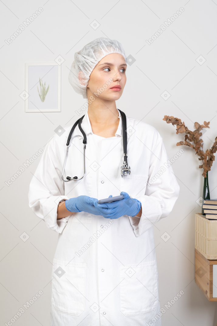 Vista frontale di una giovane dottoressa con lo stetoscopio che tiene il suo telefono
